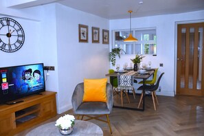 Un salon moderne avec une télévision, une horloge et un coin repas comprenant une table et des chaises.