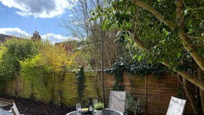 A patio with a round table, four chairs, a potted plant, and a bottle of wine.