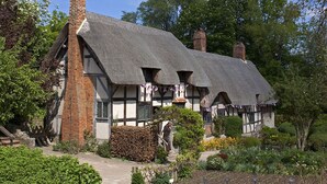A traditional half-timbered house with a thatched roof, surrounded by a well-maintained garden.