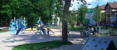 Ein Spielplatz mit Klettergerüsten und Rutschen, umgeben von Bäumen und einem befestigten Bereich.