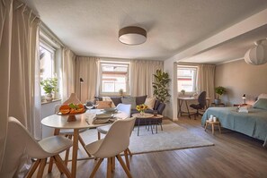 Una habitación moderna y bien iluminada con comedor, sofá, cama y escritorio.