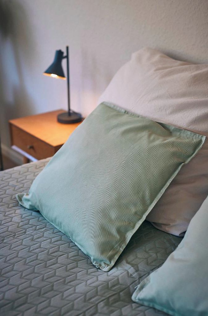 A bed with a patterned bedspread, a green pillow, and a white pillow.