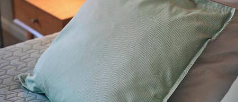 A bed with a patterned bedspread, a green pillow, and a white pillow.