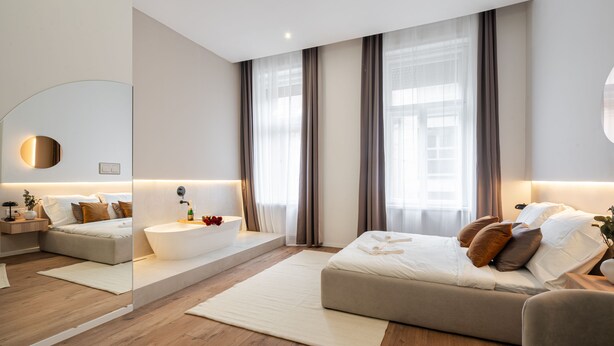 Ein modernes Schlafzimmer mit einem großen Bett, einer Sitzecke mit einer Couch, einer integrierten Badewanne und einem großen Spiegel.
