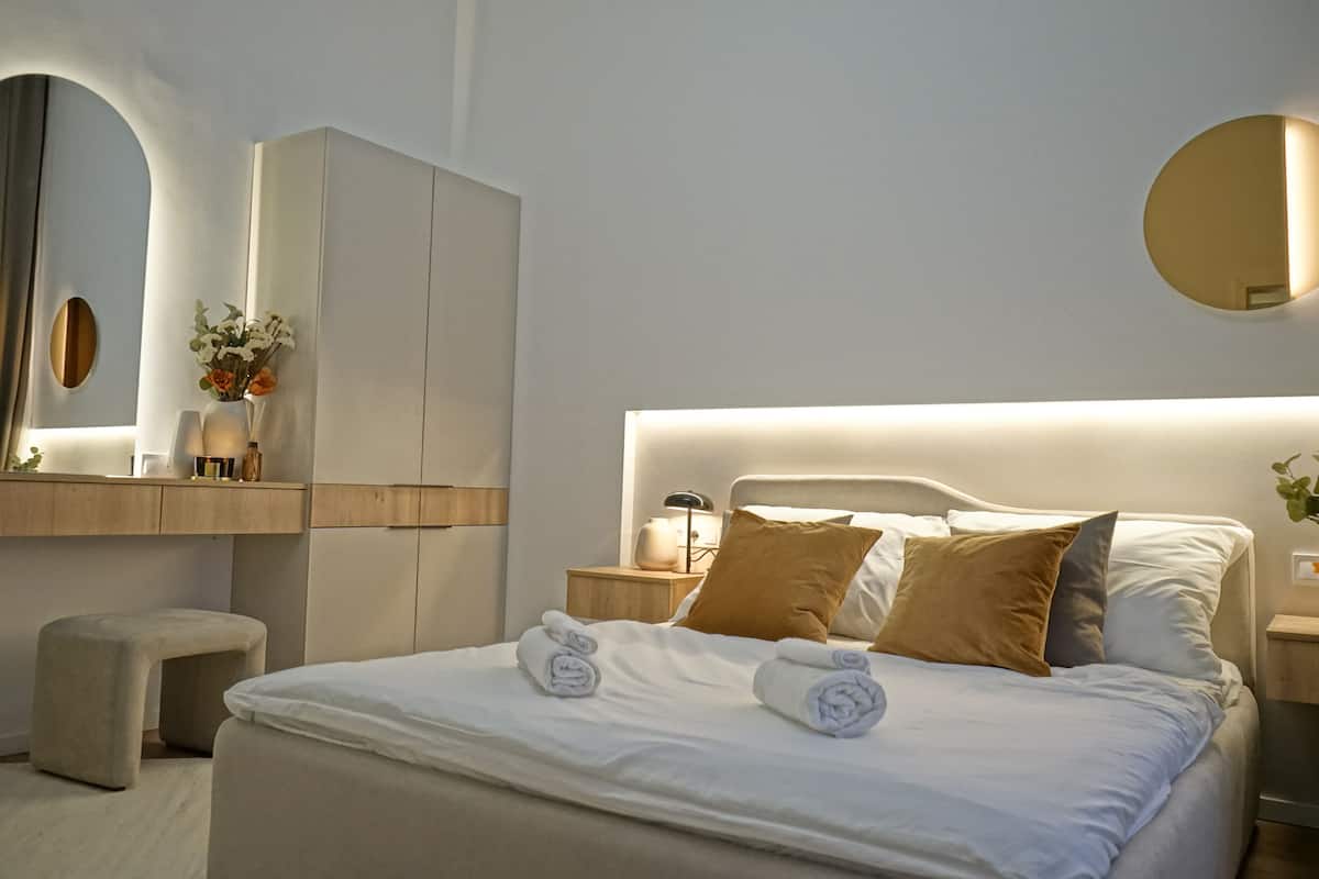 Une chambre d’hôtel moderne avec un grand lit, une table de chevet avec une lampe, une commode, un miroir et une armoire.