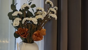 Eine weiße Vase mit Blumen auf einer Fensterbank.