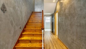 A wooden staircase with a white balustrade leading to a room with a concrete wall and a door. - Forest Villas Guest House (Leiria)