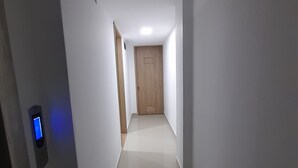 A narrow, well-lit hallway with a wooden door at the end, a wall-mounted intercom, and a tiled floor. - Granada suites aparta estudio (Cali)