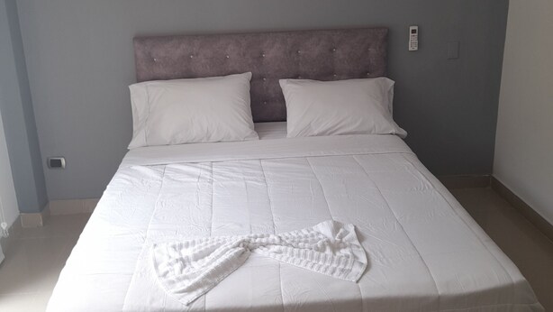 A neatly made bed with a white duvet and a white throw blanket, a headboard, and a wall-mounted phone. - Granada suites aparta estudio (Cali)