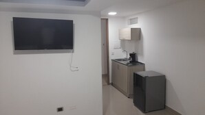 A compact kitchen with a built-in stove, a sink, and a microwave. A flat-screen TV is mounted on the wall. - Granada suites aparta estudio (Cali)