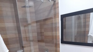A bathroom with a glass-enclosed shower, a white toilet, and a mirror above the sink. - Granada suites aparta estudio (Cali)