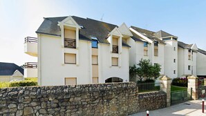 A multi-story residential building with a stone wall in front, balconies, and a clear sky. - Le kervenel - les gîtes de la Côte d'Amour (Le Croisic)