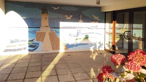 A mosaic mural of a lighthouse, a glass door entrance, and potted flowers. - Le kervenel - les gîtes de la Côte d'Amour (Le Croisic)