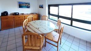 A dining area with a round table and six wooden chairs, a wooden cabinet, and a window with a view. - Le kervenel - les gîtes de la Côte d'Amour (Le Croisic)