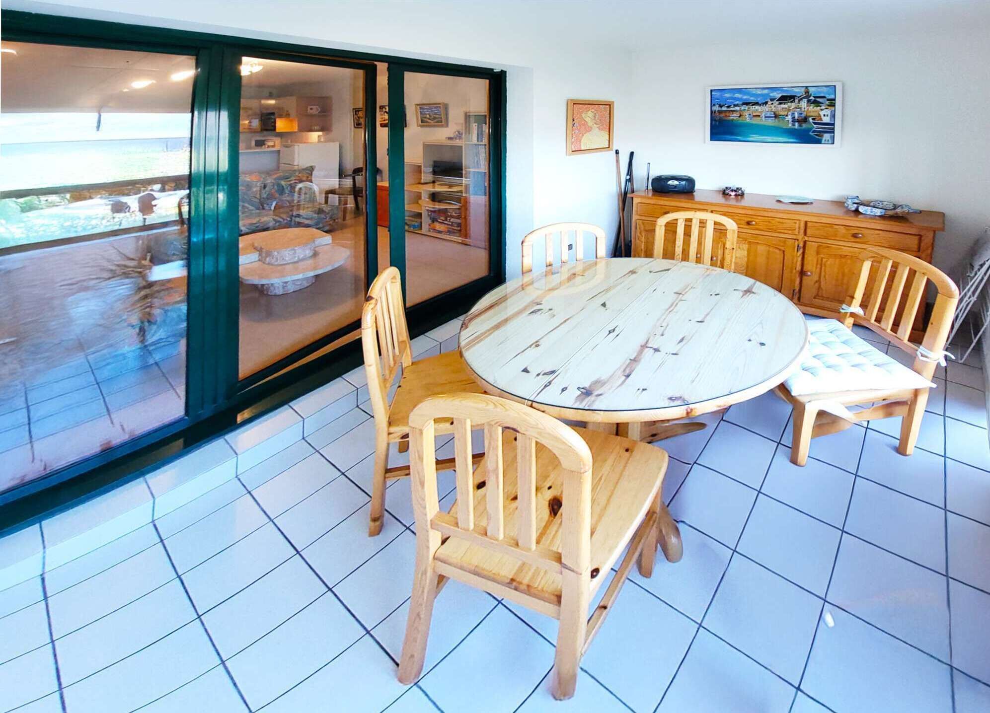 A dining area with a round table and wooden chairs, a wooden cabinet, and a sliding glass door leading to a balcony.
