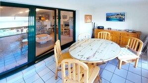 A dining area with a round table and wooden chairs, a wooden cabinet, and a sliding glass door leading to a balcony. - Le kervenel - les gîtes de la Côte d'Amour (Le Croisic)