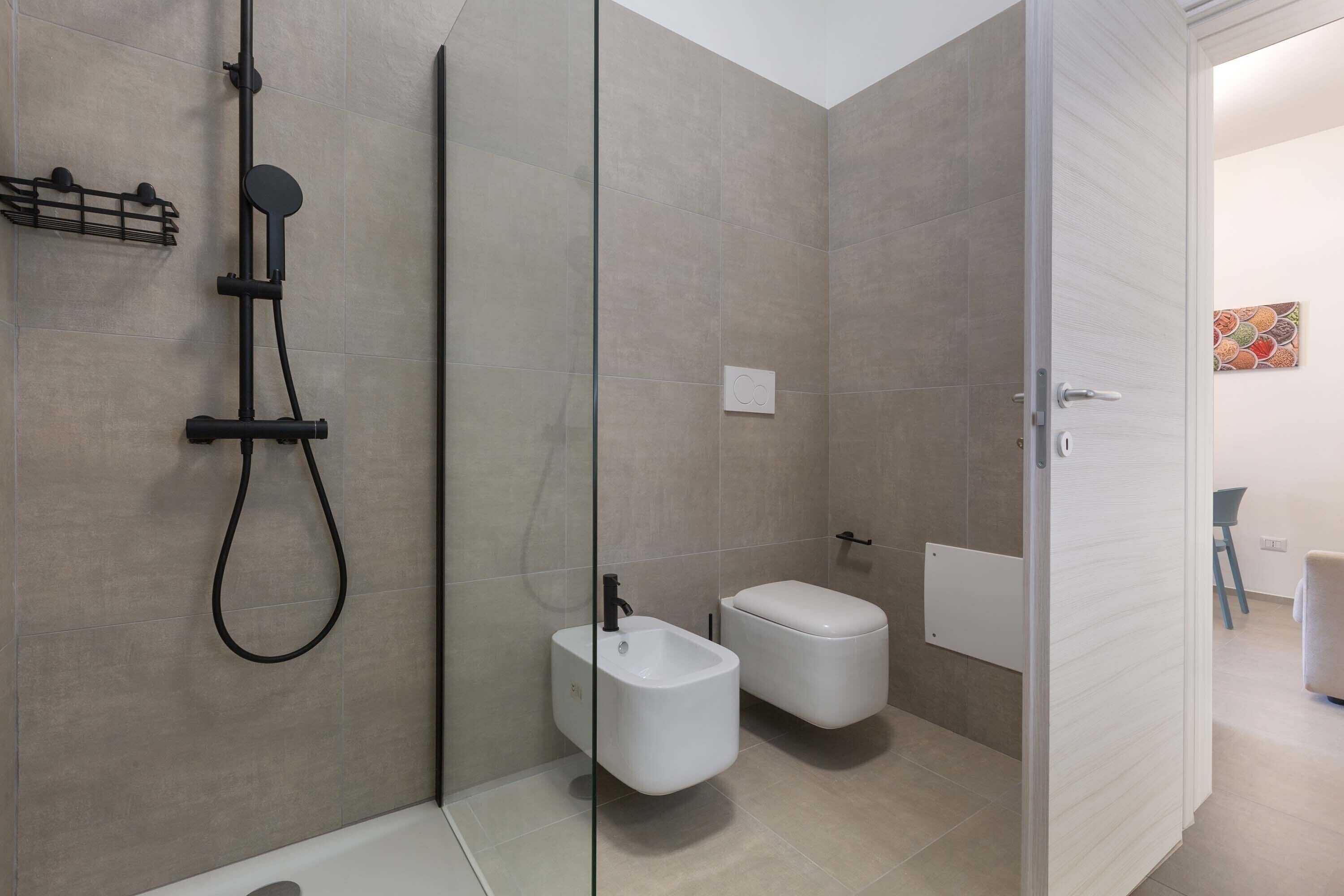 A modern bathroom with a glass shower enclosure, a toilet, and a bidet.