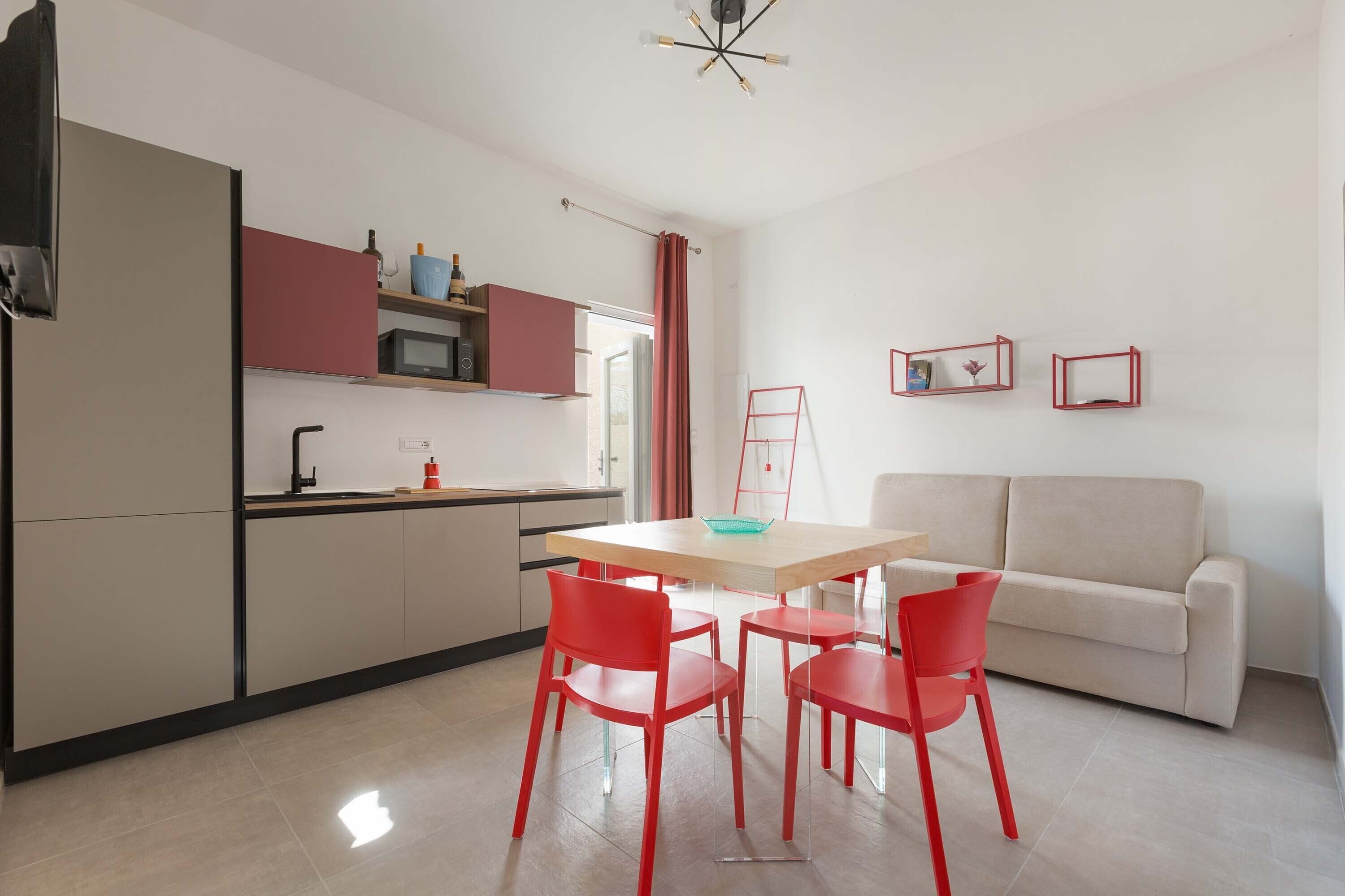 A compact living space with a kitchenette, a dining area with red chairs, and a sofa.