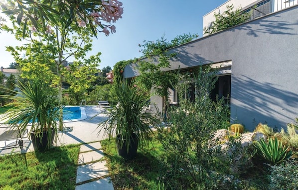 Una casa moderna con piscina, rodeada de exuberante vegetación y diversas plantas.