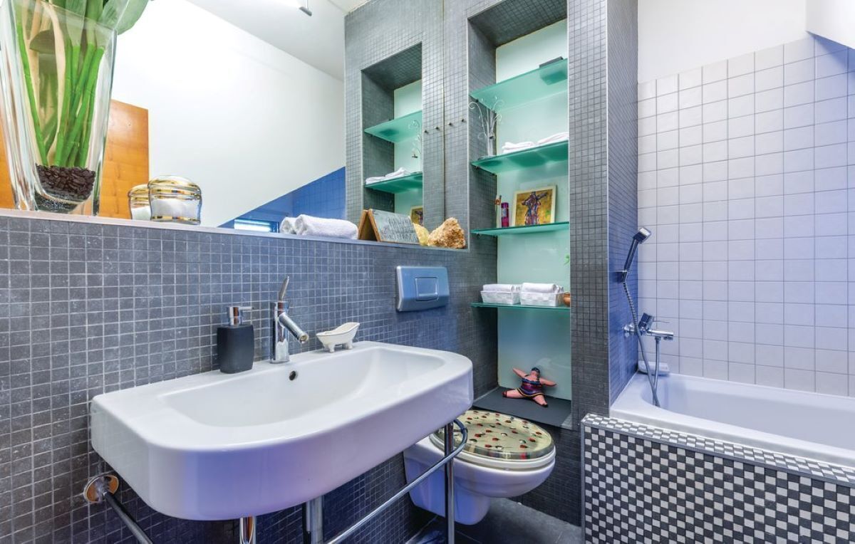 Un bagno moderno con un lavandino grande, un water e una vasca da bagno. Sono presenti scaffali con articoli da toilette e oggetti decorativi.