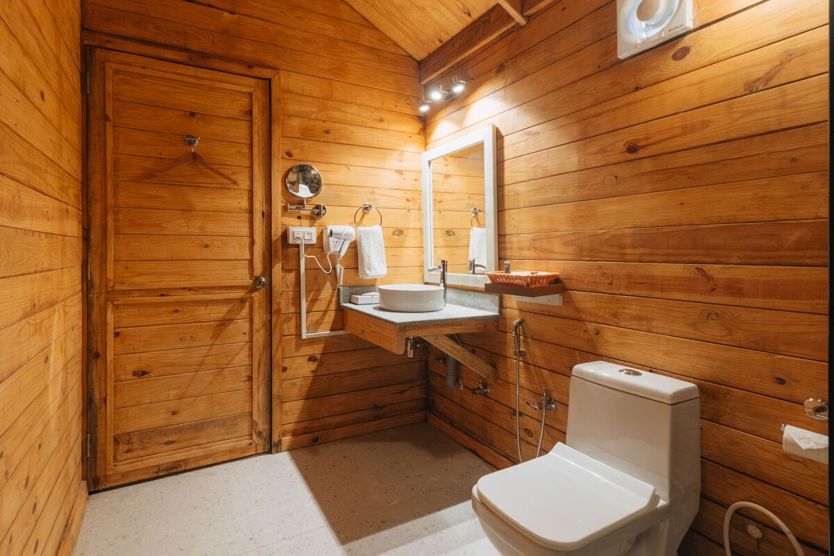 A wooden-paneled bathroom with a toilet, sink, mirror, towel rack, and a door.