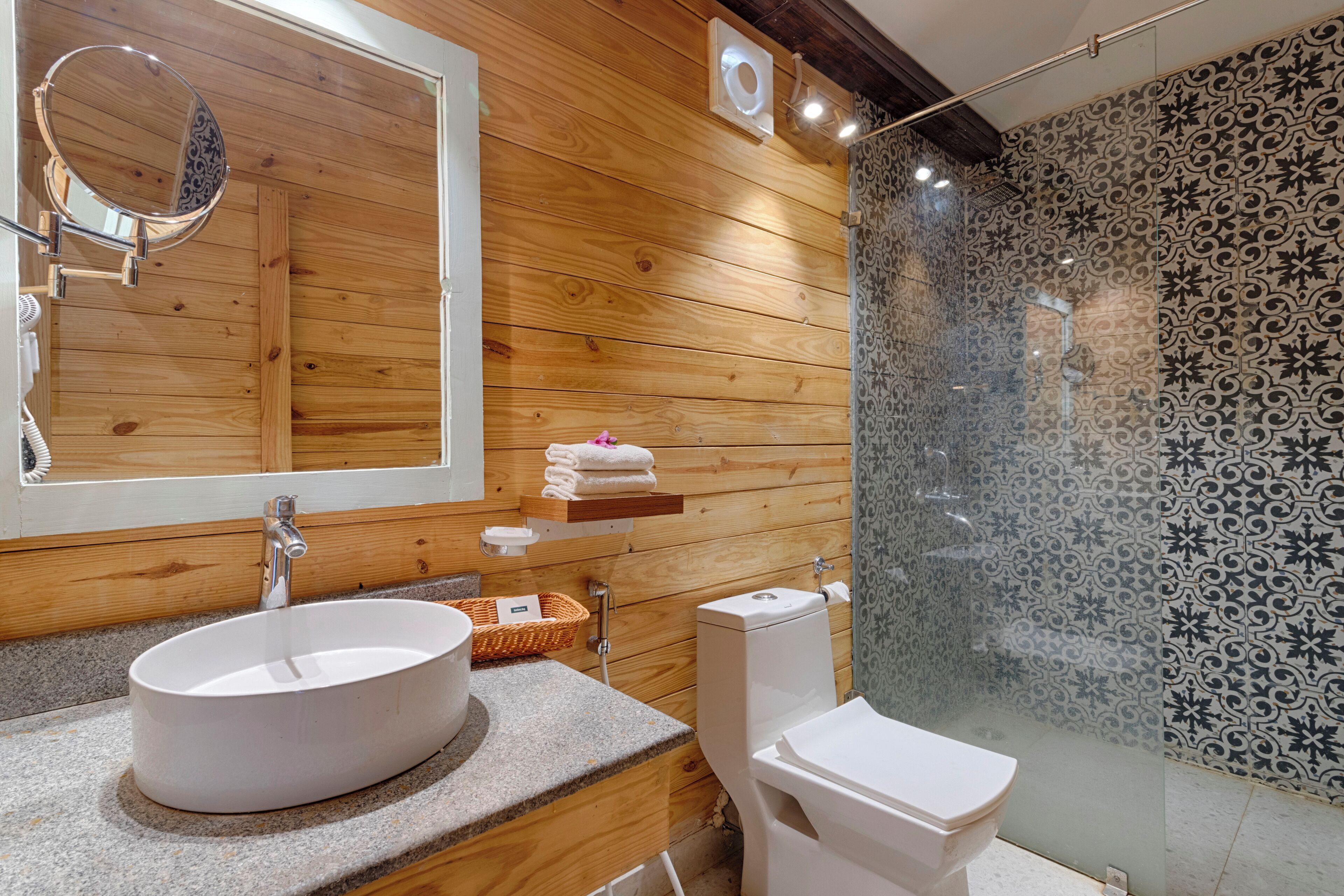 A modern bathroom with a wooden panel wall, a round mirror, a white sink, and a glass-enclosed shower area.