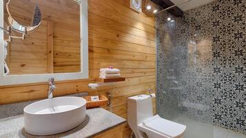 A modern bathroom with a wooden panel wall, a round mirror, a white sink, and a glass-enclosed shower area.