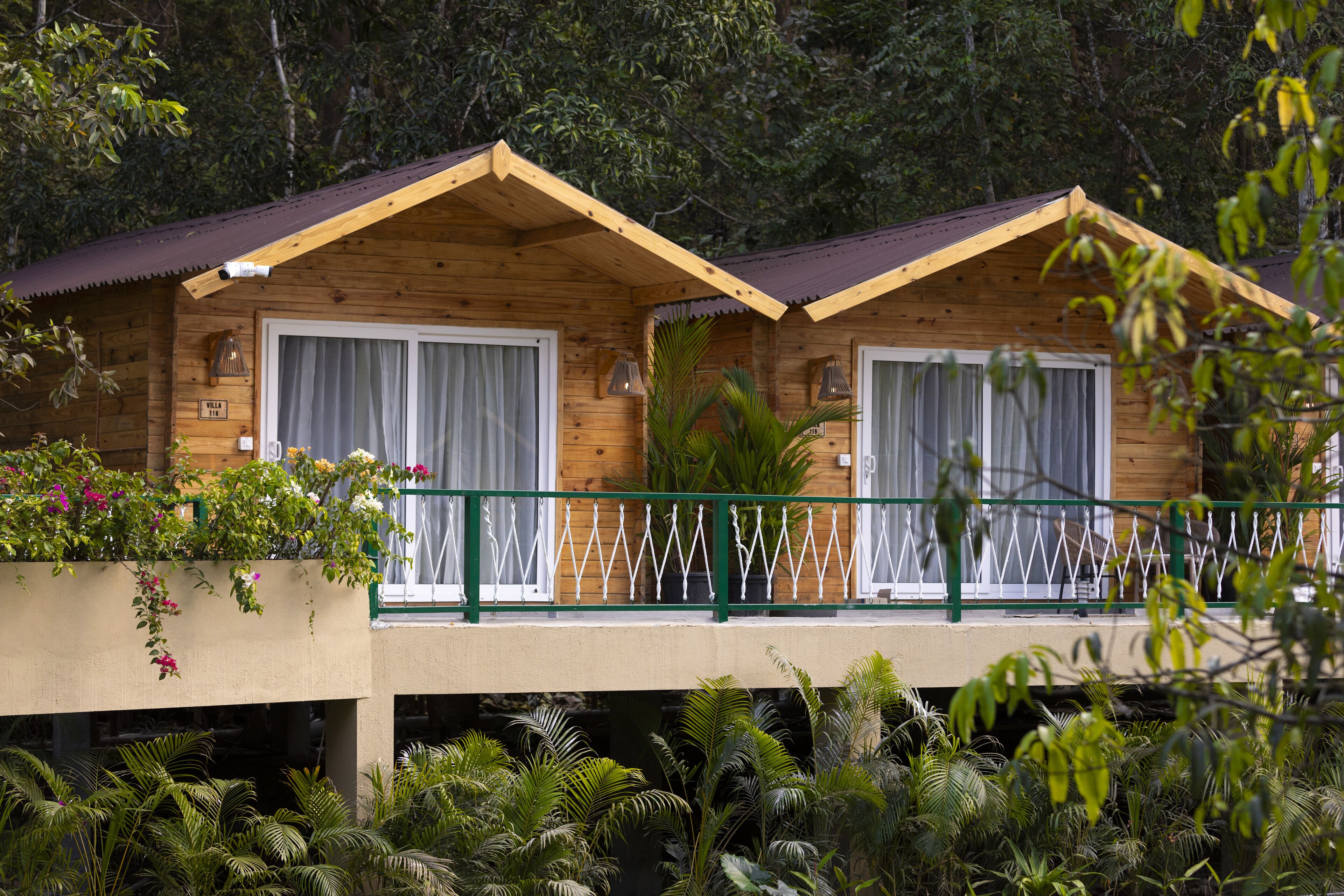 A wooden cabin with two bedrooms, each with a balcony and a window with curtains.