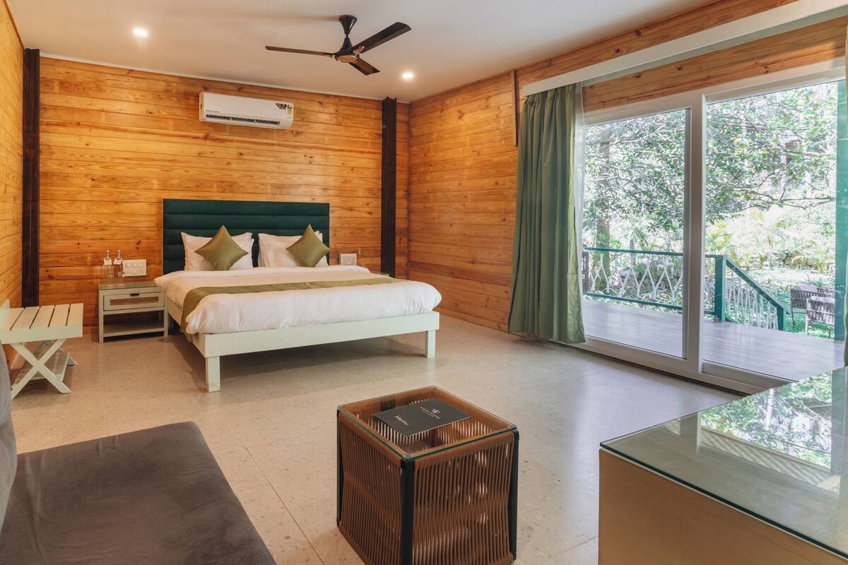 A bedroom with a bed, a nightstand, a glass coffee table, a sofa, and a view of the outdoors.