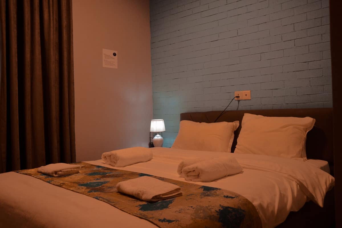 Una habitación de hotel con una cama, una mesita de noche, una lámpara y una pared de ladrillo.