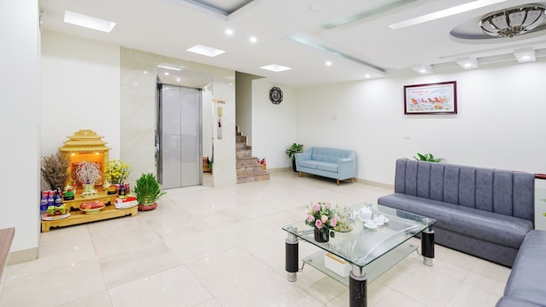 A modern living room with a glass coffee table, a grey sofa, and a small altar with offerings. - New An Phú Hotel (Hanoi)