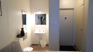 A small, clean room with a bed, a bedside table, a chair, a sink, and a mirror. - Hotelli Immalanjärvi (Imatra)