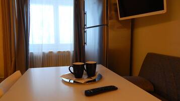 A hotel room with a bed, a TV mounted on the wall, and a table with two cups and a remote control.