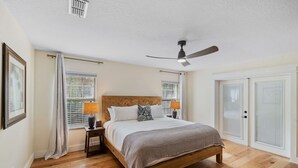 Ein Schlafzimmer mit einem hölzernen Bett, zwei Nachttischlampen, einem Deckenventilator und einem großen Fenster mit Jalousien.
