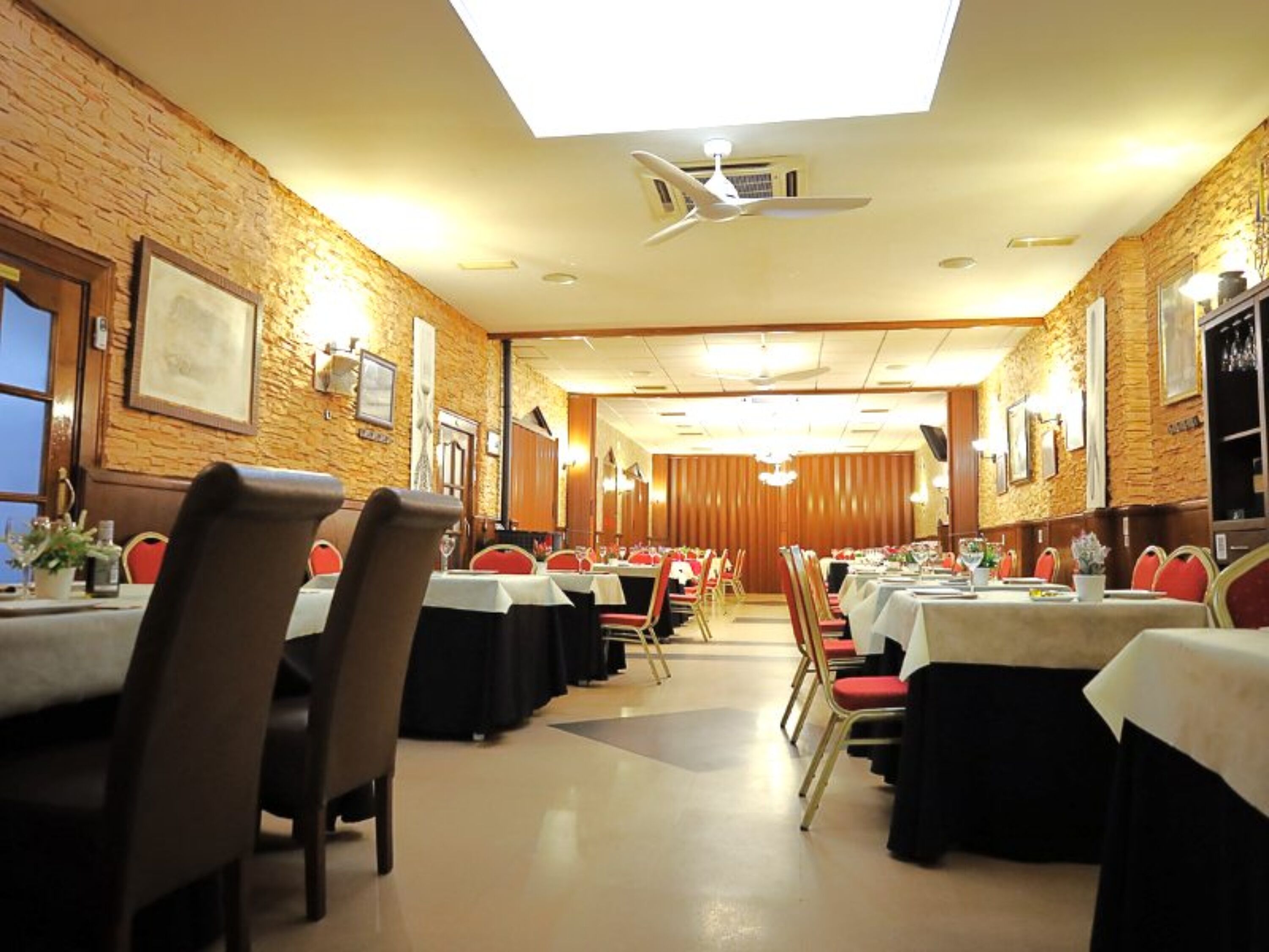 A conference room with tables and chairs, a ceiling fan, and a brick wall.