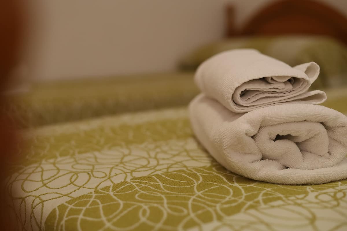 A neatly folded white towel on a bed with a green patterned bedspread.