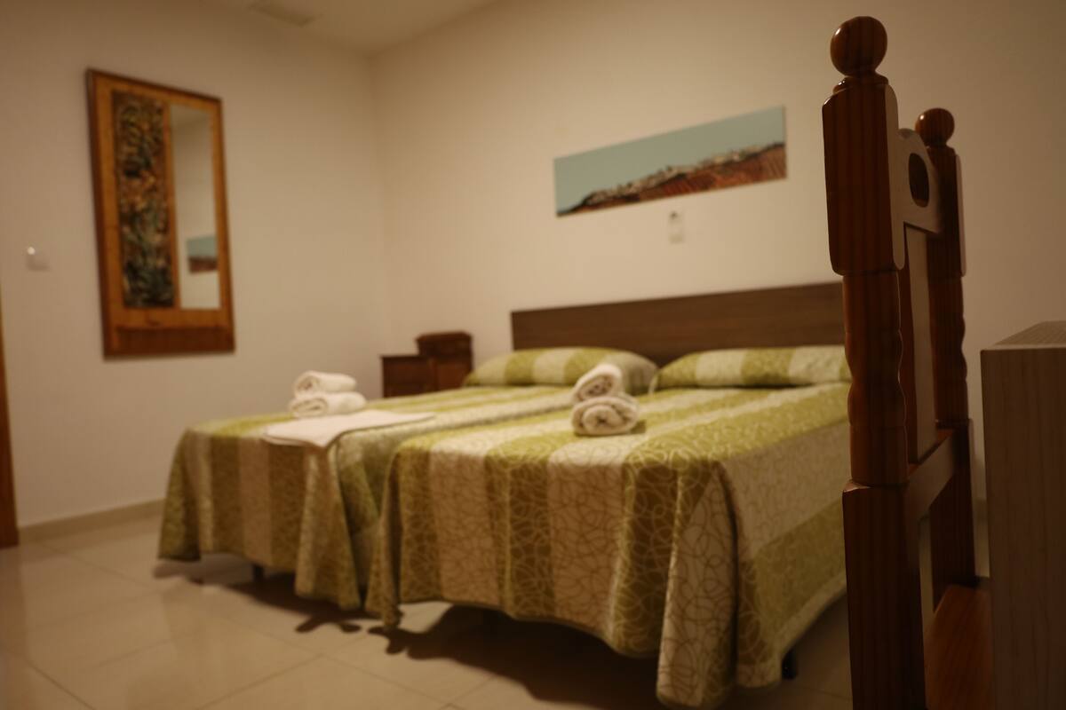 A hotel room with two beds, a wooden headboard, a painting on the wall, and a small nightstand.