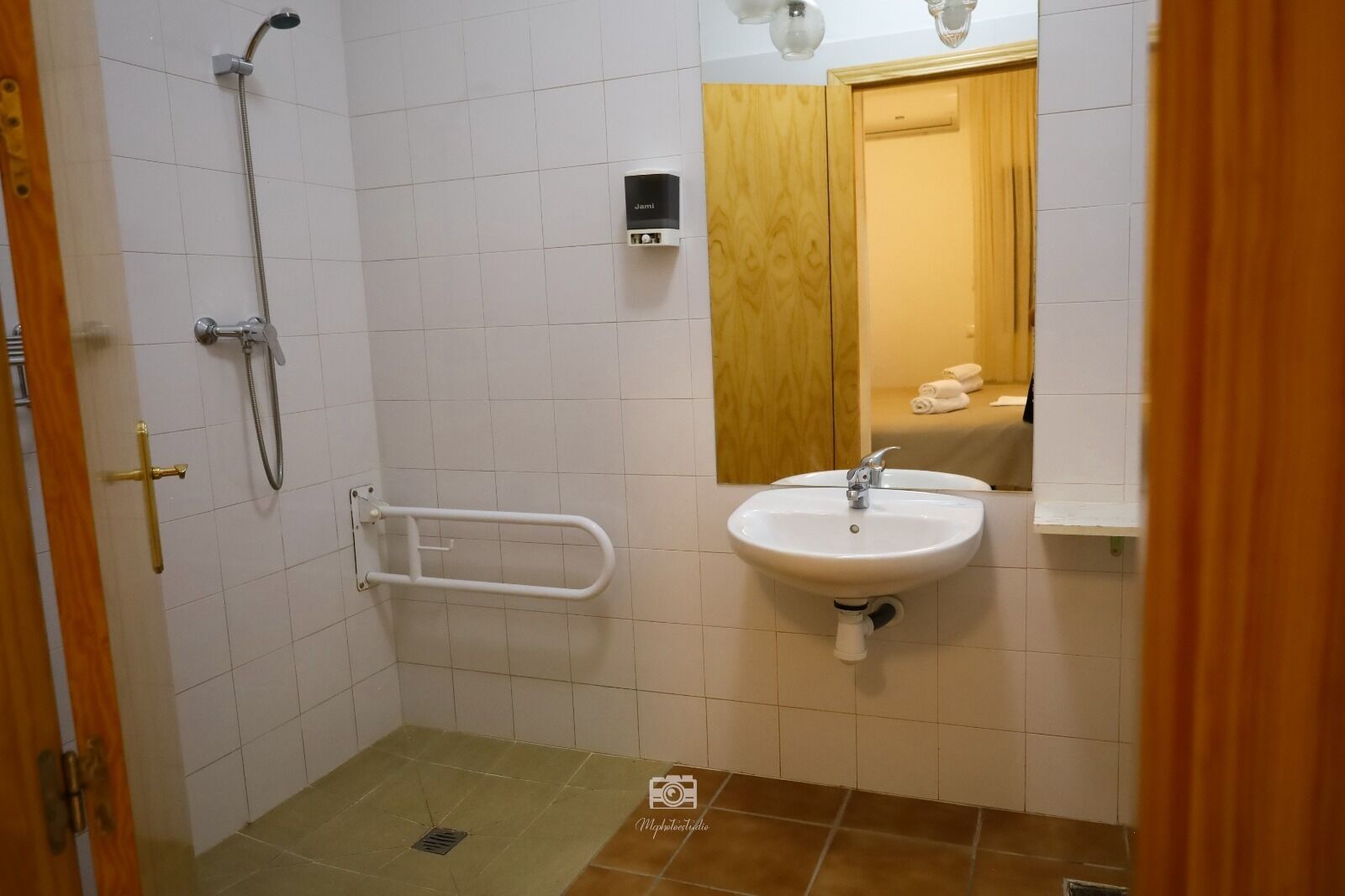 A bathroom with a shower, a sink, and a handrail.