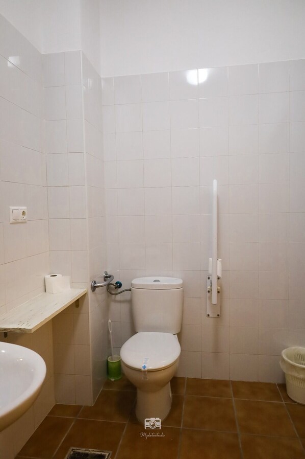 A bathroom with white tiles, a toilet, a sink, and a trash bin.