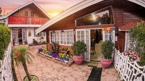 A two-story wooden building with a balcony, large windows, and a garden area with potted plants and flowers. - Recanto Monte Suíço (Campos do Jordão)