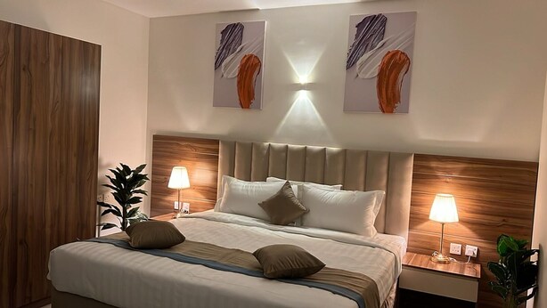 Una habitación de hotel con una cama grande, dos mesitas de noche con lámparas, un cabecero de madera y dos cuadros abstractos en la pared.
