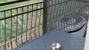 Un balcon avec une balustrade en métal, une table et un cendrier en métal.