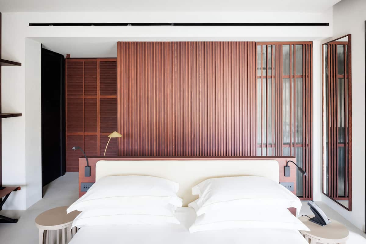 A modern bedroom with a large bed, wooden panel headboard, bedside tables, and a ceiling fan.