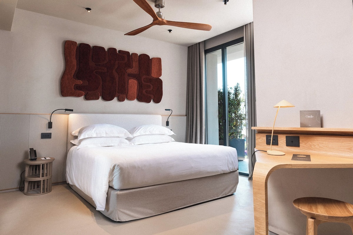 A modern bedroom with a large bed, a ceiling fan, a bedside table, and a desk with a lamp.