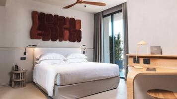 A modern bedroom with a large bed, a ceiling fan, a bedside table, and a desk with a lamp.