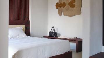 Une chambre moderne avec un cadre de lit en bois, un ventilateur de plafond, une œuvre d’art abstraite accrochée au mur et une table de chevet sur laquelle se trouve un sac à main.