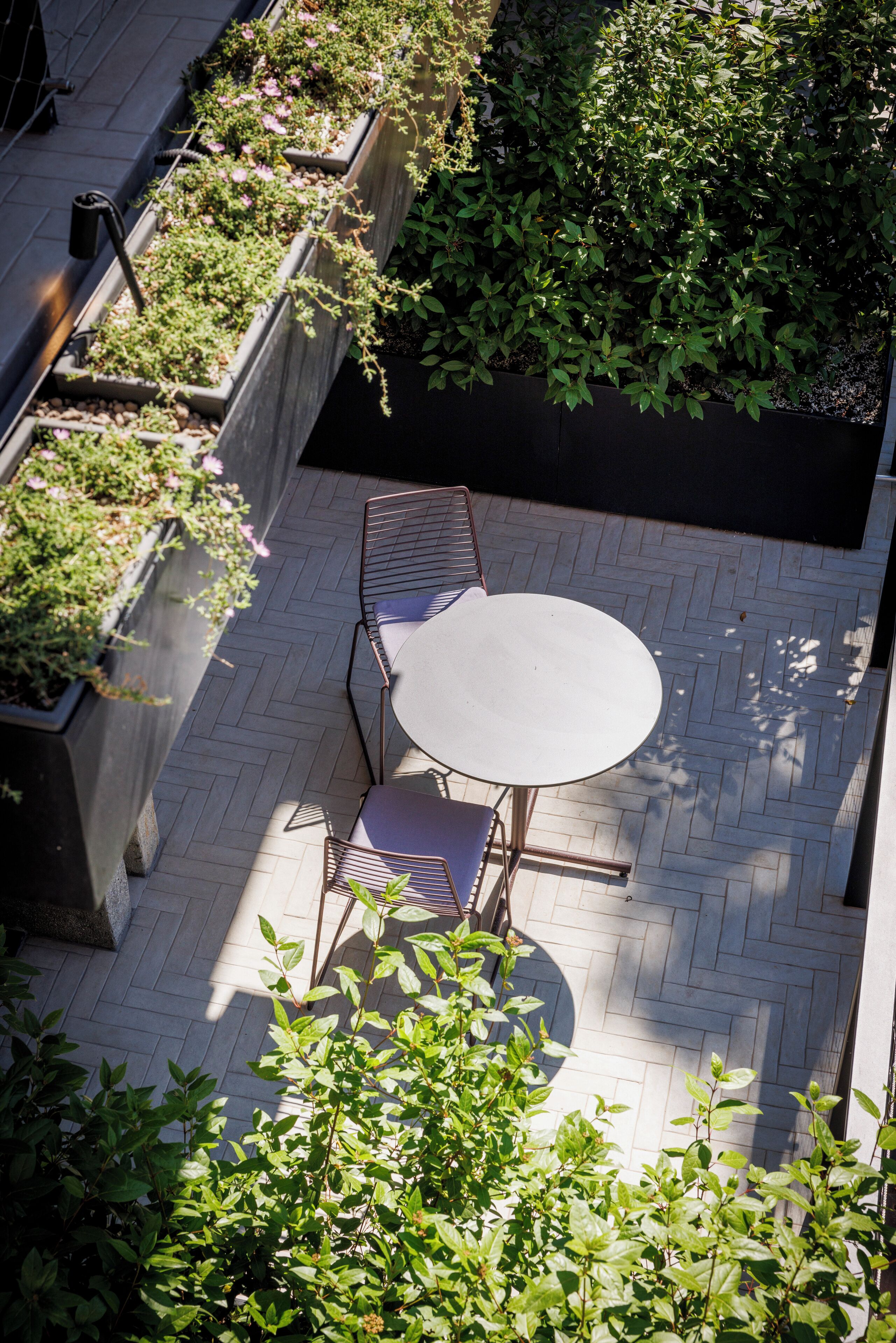 Una terrazza sul tetto con un tavolo rotondo e sedie, circondata da fioriere con piante verdi.