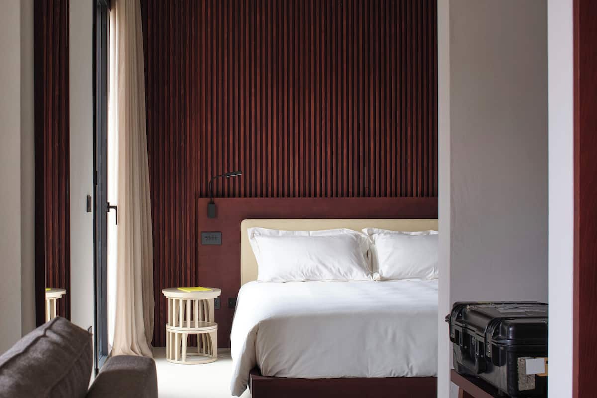 A hotel room with a bed, a small table, a chair, and a suitcase.