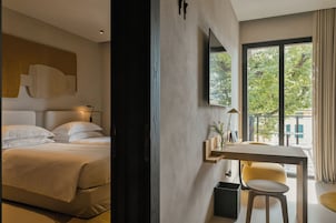 Moderni hotellihuone, jossa on sänky, työpöytä ja suuri ikkuna, josta avautuu näkymä vehreään maisemaan.