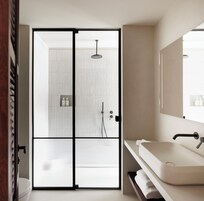 A modern bathroom with a sliding glass door leading to a shower area, a white sink, and a large mirror.